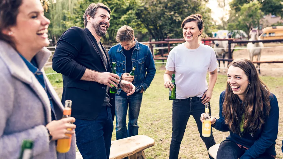 Group of friends laughing outdoors holding drinks.