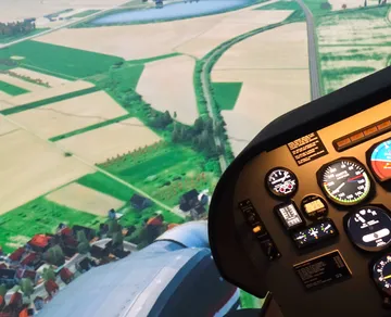Flight simulator cockpit over rural landscape.