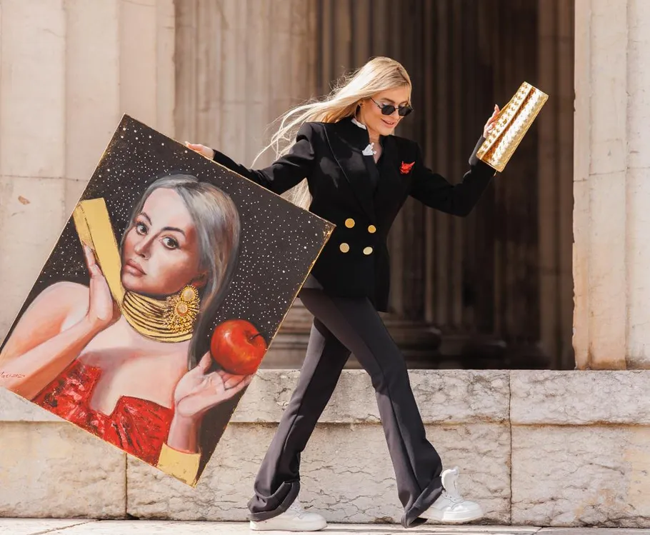Woman holds a painting and rectangular object outdoors.