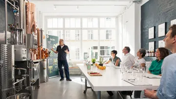 Person erklärt Brennereiausrüstung einer sitzenden Gruppe.