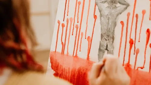 Person painting abstract figure with red lines.
