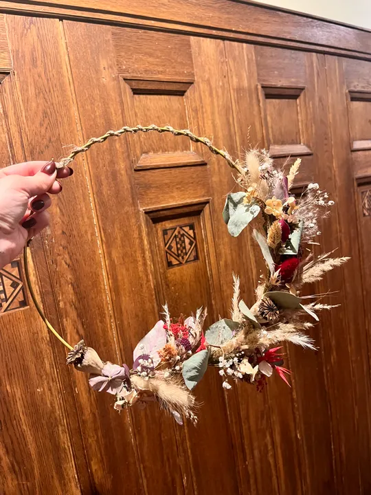 Hand holding floral wreath, wooden background.