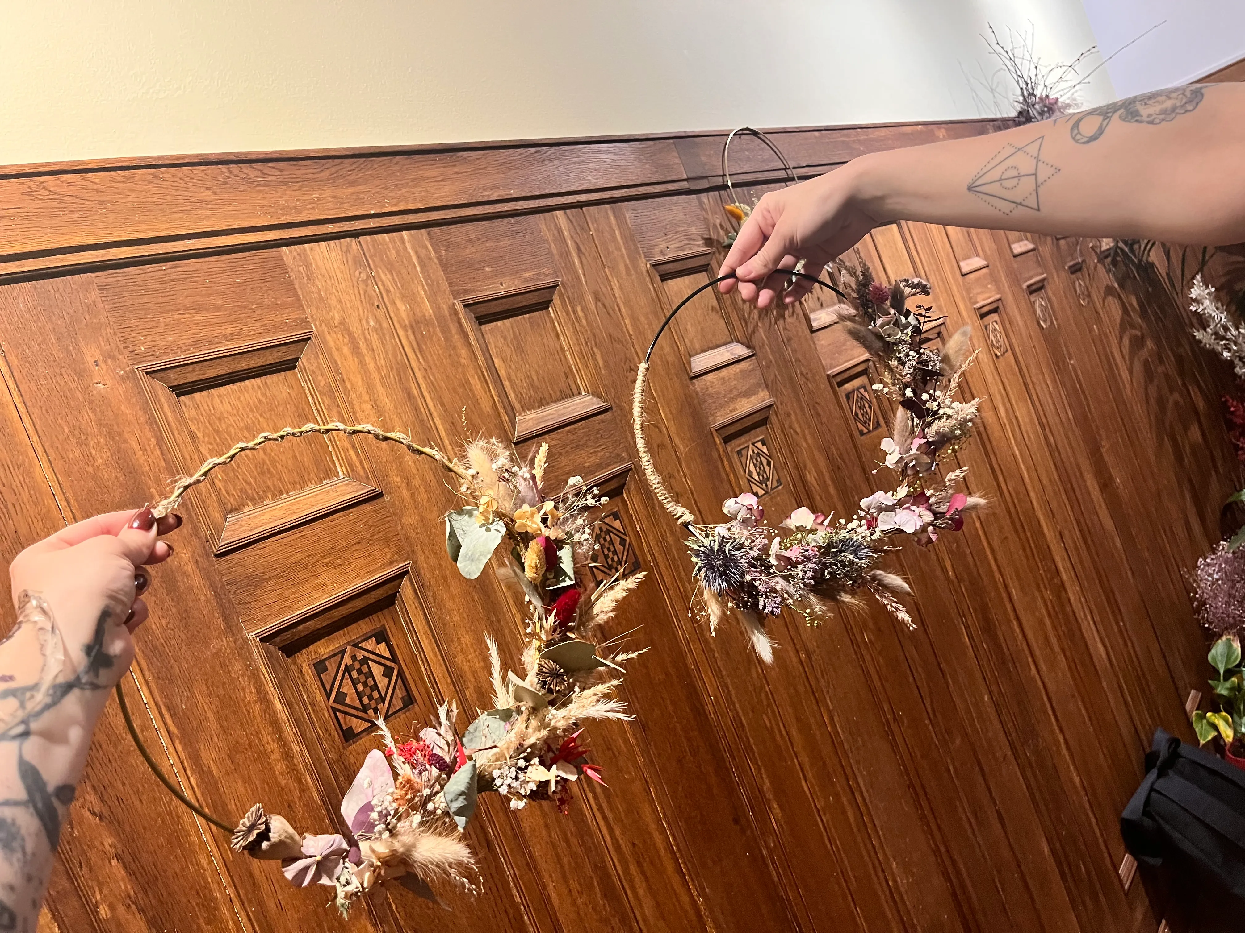 Hands hold floral wreaths against wooden wall.