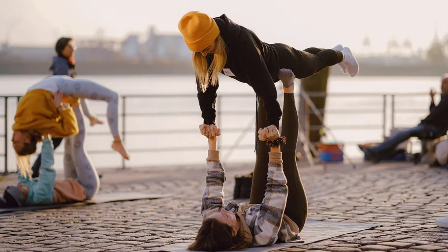 People practicing acro yoga by the waterfront.