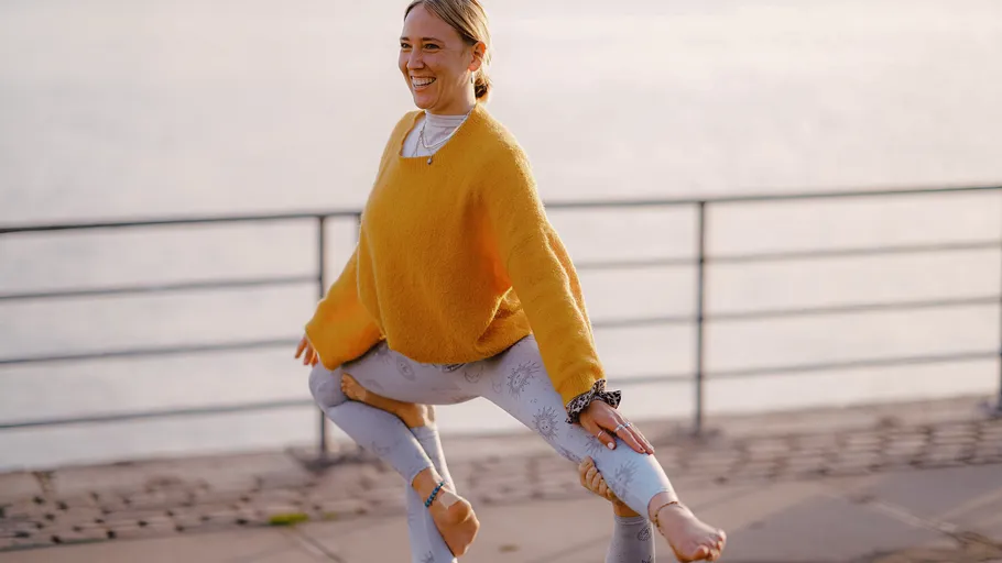 Woman in yoga pose outdoors by water.