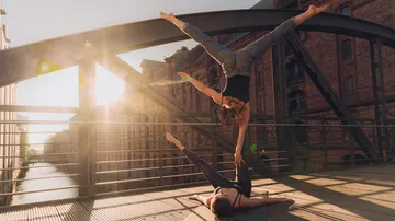 Zwei Personen machen Akroyoga auf einer Brücke.