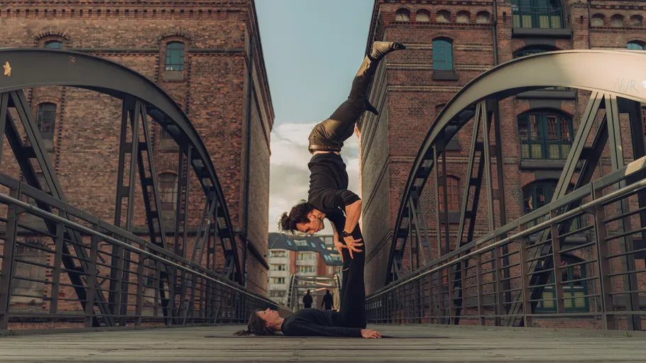 Zwei Personen machen Akrobatikpose auf Brücke.