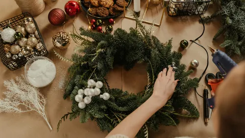 Person crafting festive wreath on table.