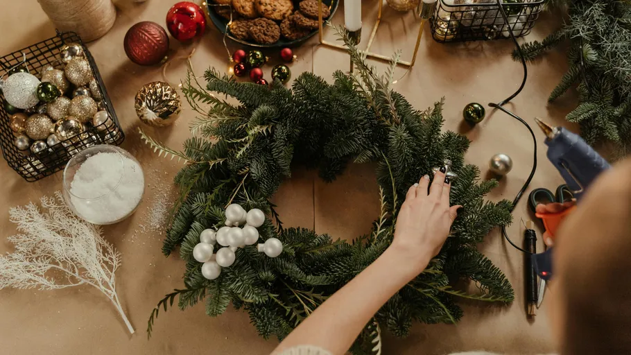 Person crafting festive wreath on table.