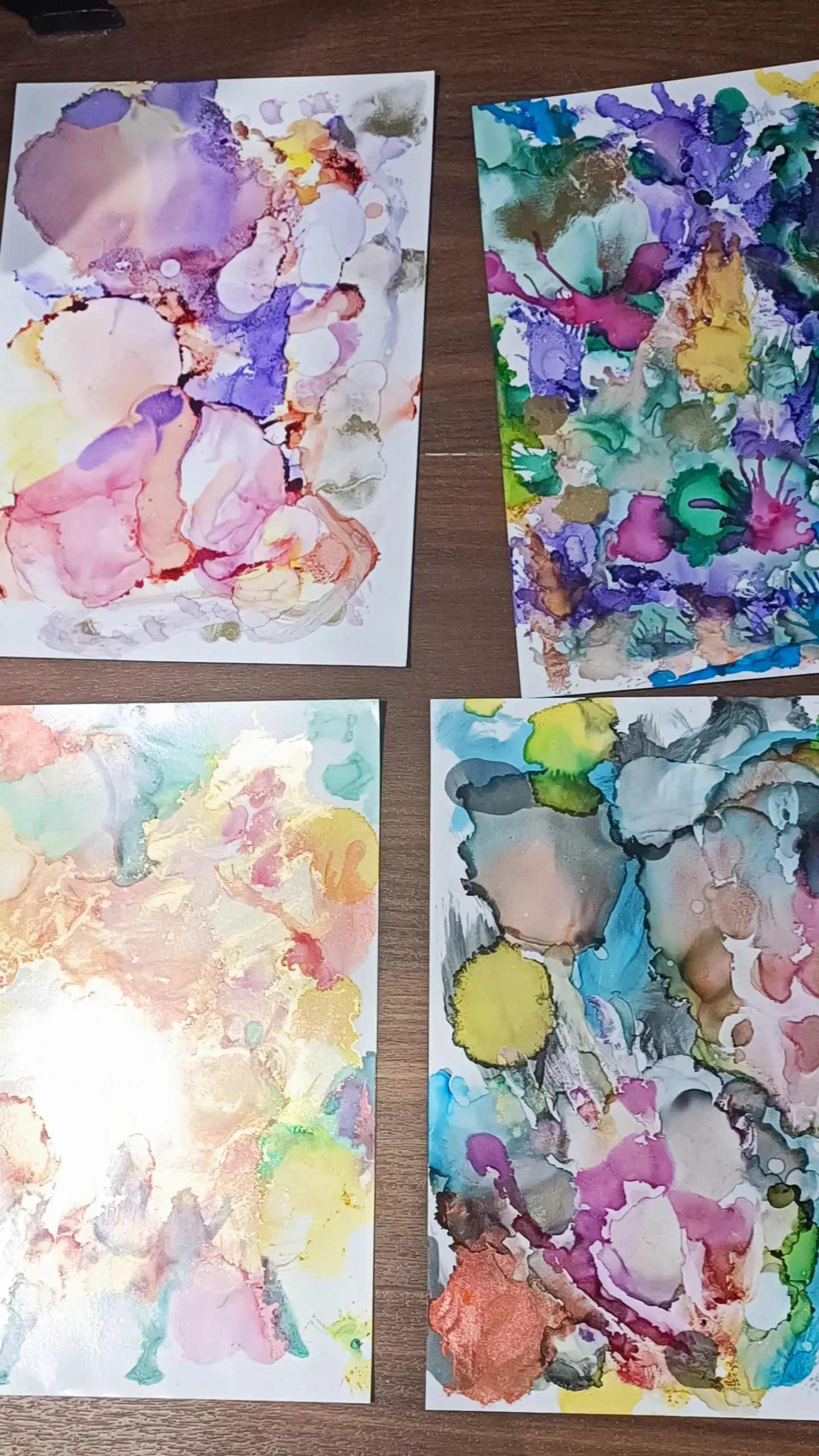 Four abstract watercolor paintings on a wooden surface.