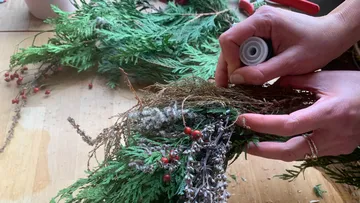 Hands arranging foliage on wooden table.