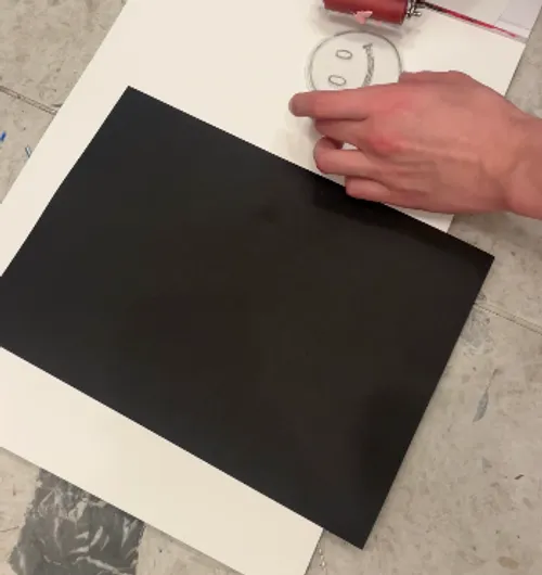 Hand drawing smiley face beside black paper.