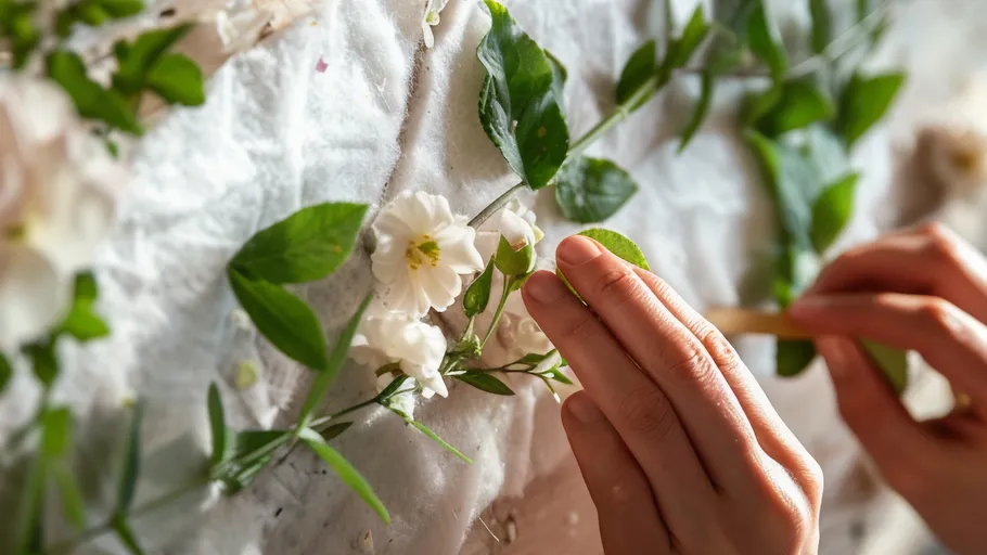 Hands arrange flowers and leaves on fabric.