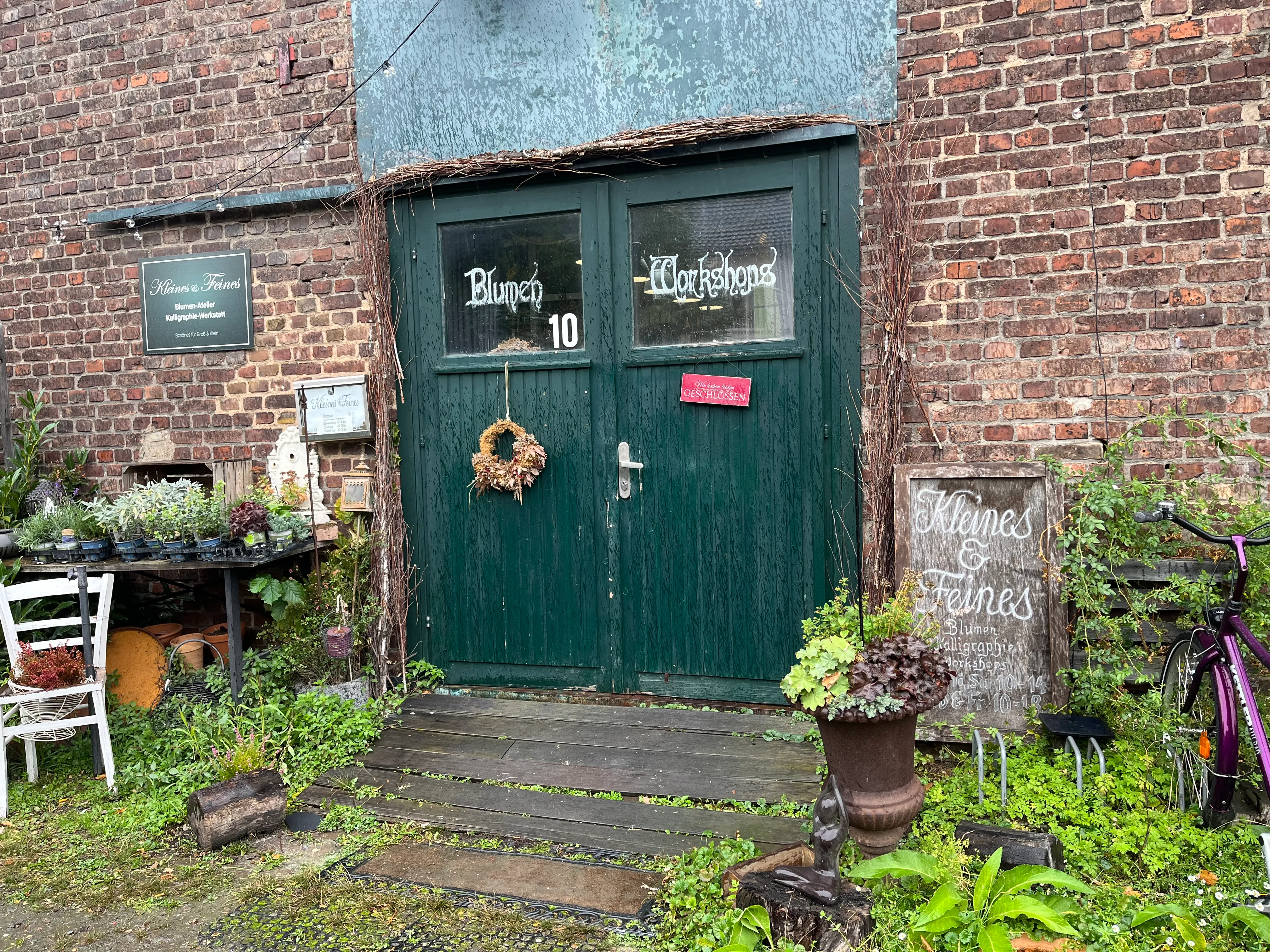 Green doors with signs, surrounded by plants.
