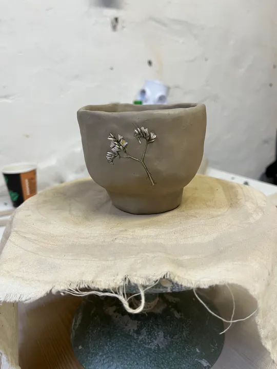 Tonbecher mit Blumenabdruck auf Tisch.