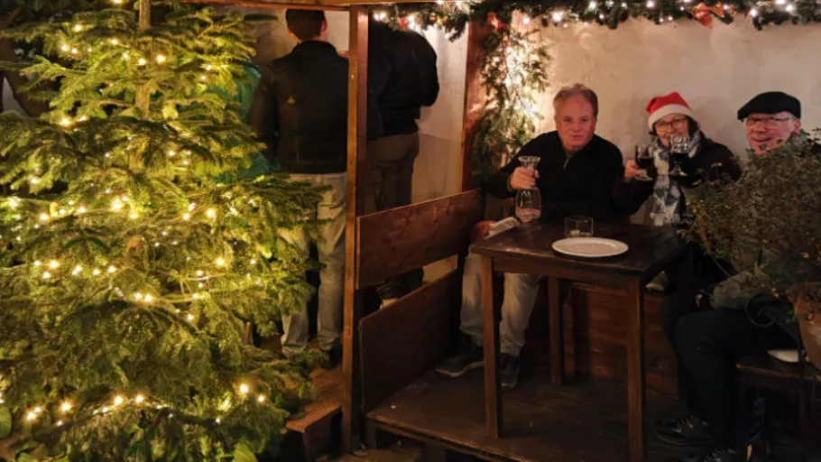 Drei Personen trinken in einem festlich geschmückten Stand.