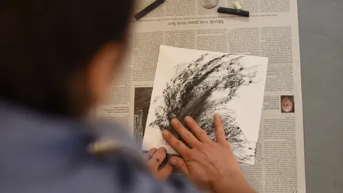 Person drawing abstract art on paper with charcoal.