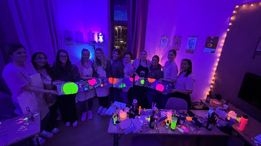 Group holding neon paintings in dimly lit room.