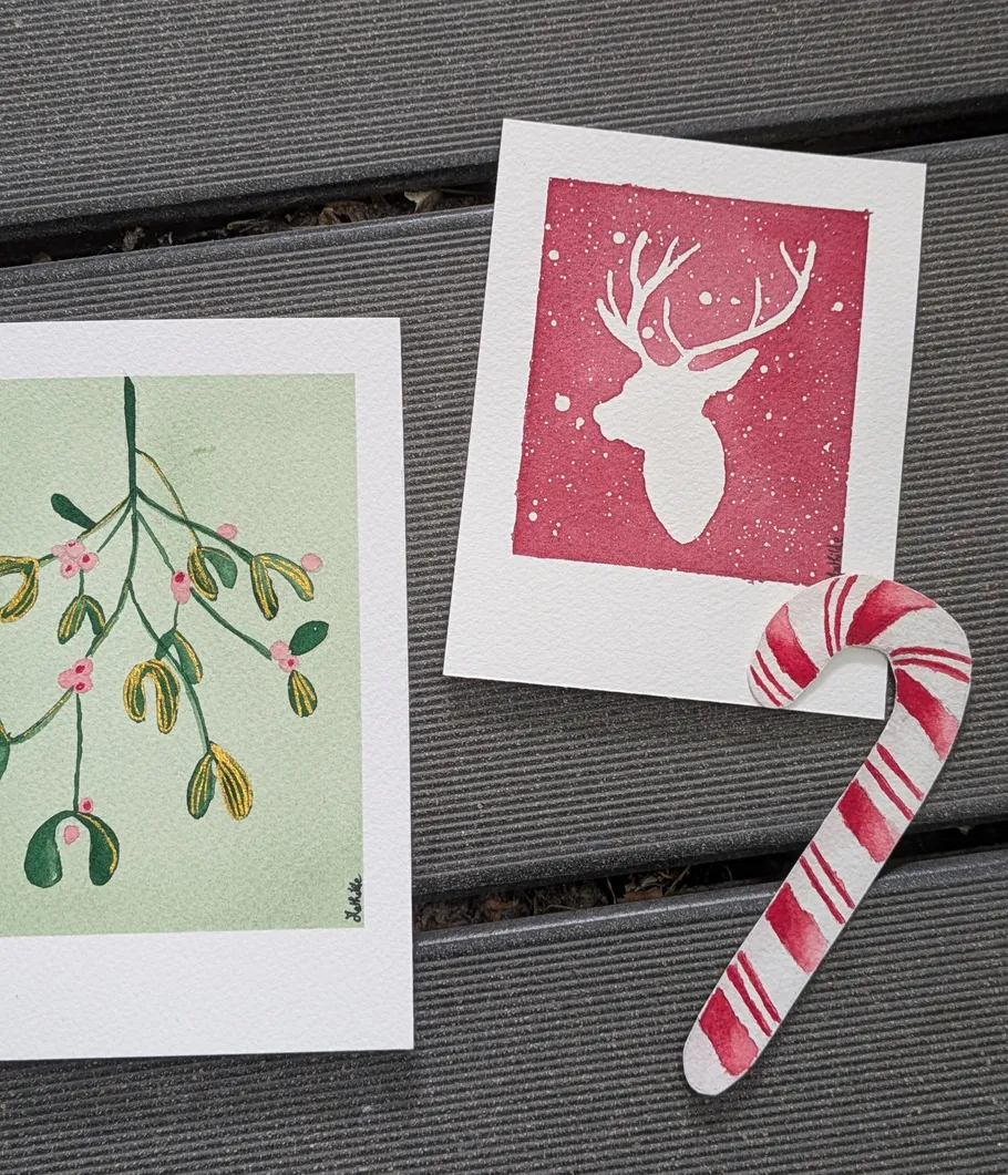 Two festive cards and candy cane on wood.