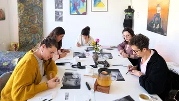 Personen zeichnen an einem Tisch im Atelier.