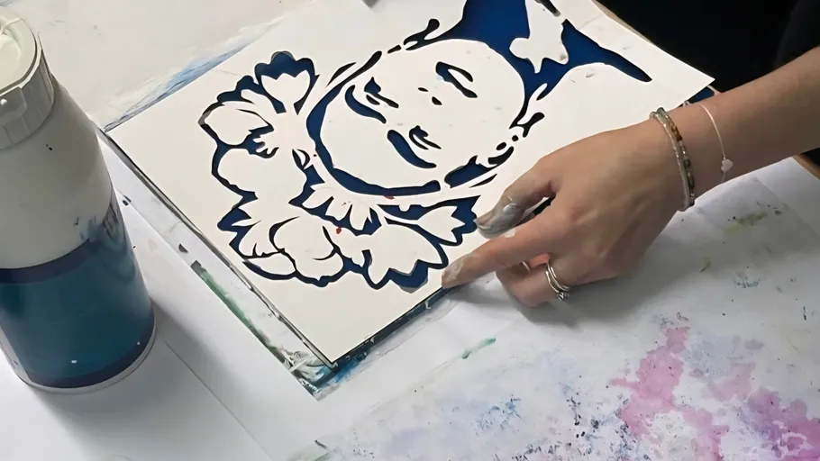 Person painting stencil image on paper.