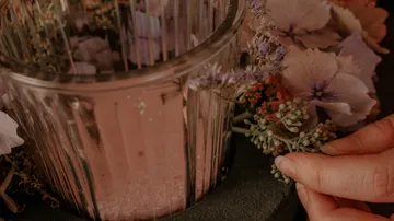 Eine Hand arrangiert Blumen um ein Glasgefäß.