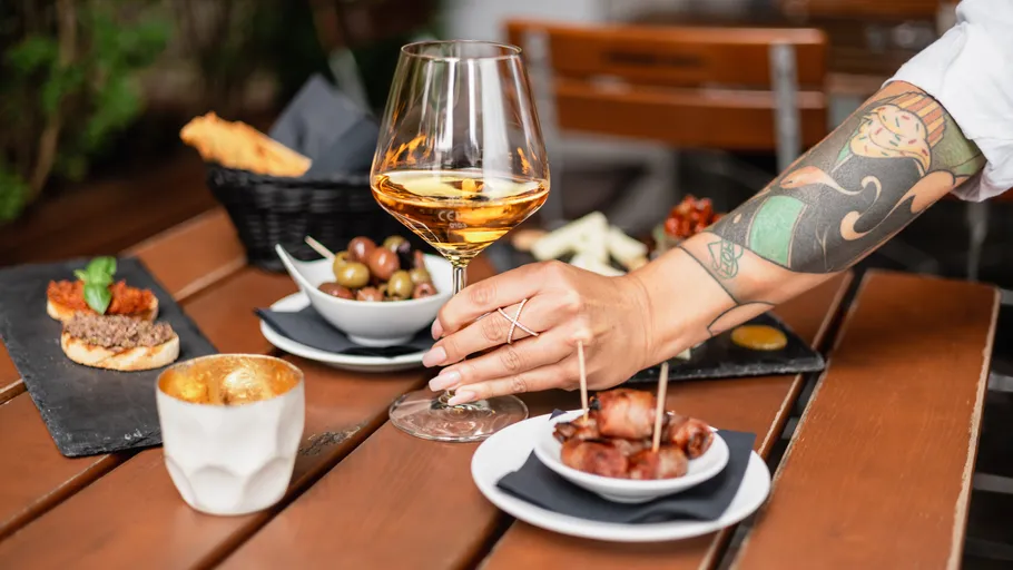 Tattooed arm holds wine glass over table snacks.
