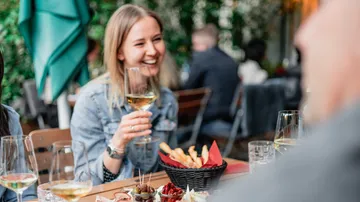 Frau genießt Wein an einem Gartencafé-Tisch.