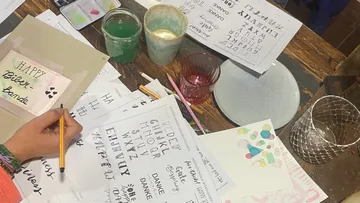 Handlettering-Übung mit verschiedenen Werkzeugen auf Tisch.