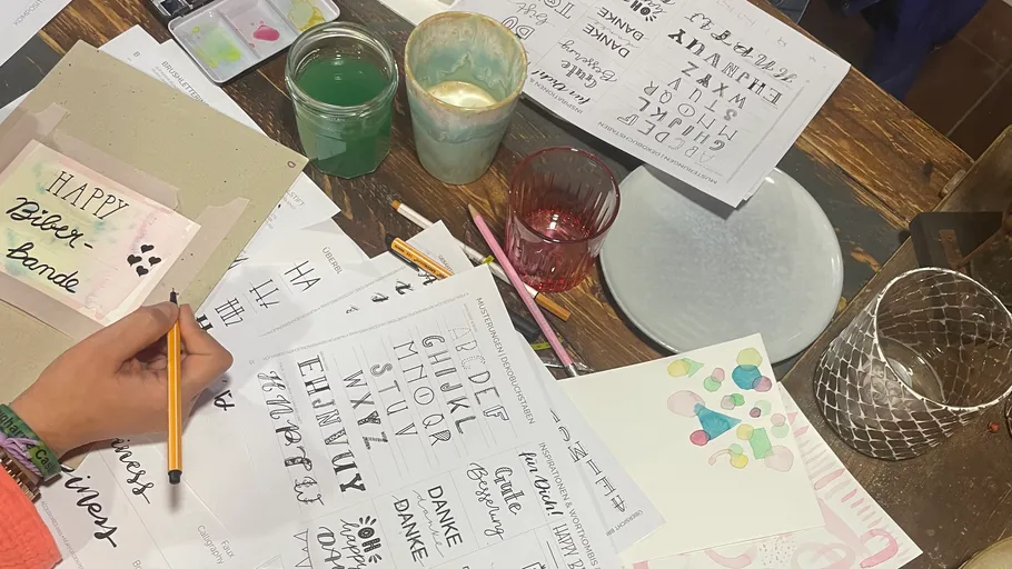 Handlettering-Übung mit verschiedenen Werkzeugen auf Tisch.