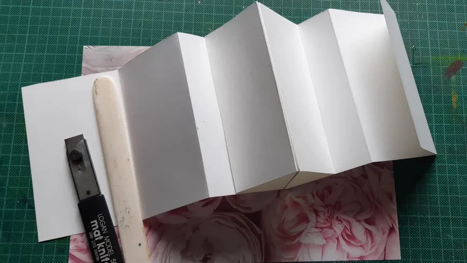 Accordion-folded paper on table with tools.