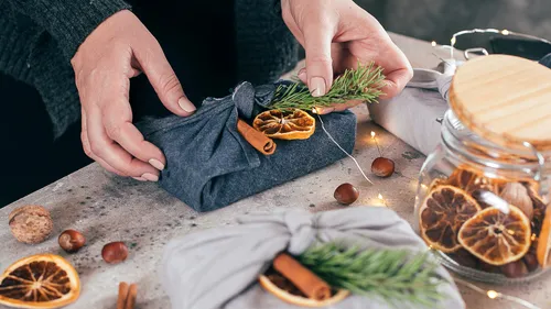 Person wrapping gift with dried orange and greenery.