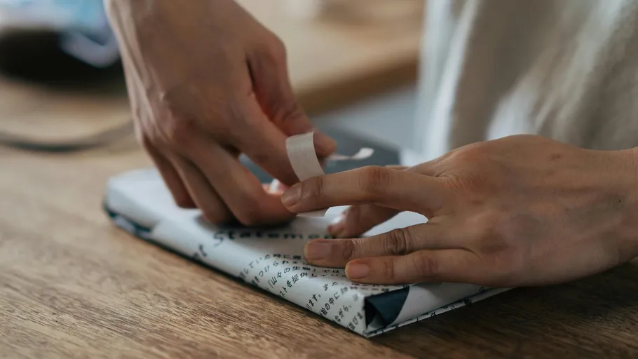 Hands wrapping a gift on table.