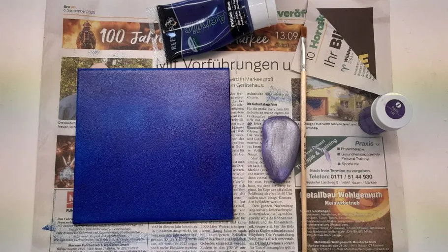 Blue canvas on newspaper with art supplies.