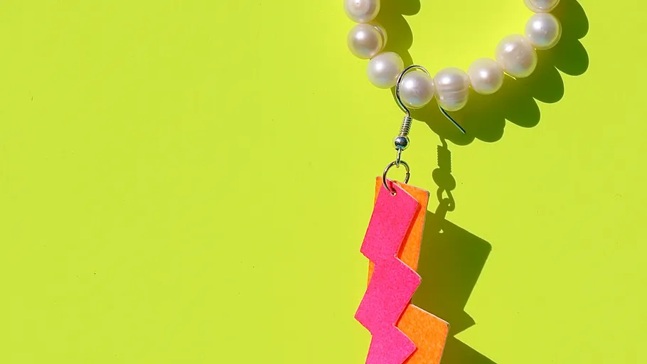 Pearl earring with pink lightning shape on green background.