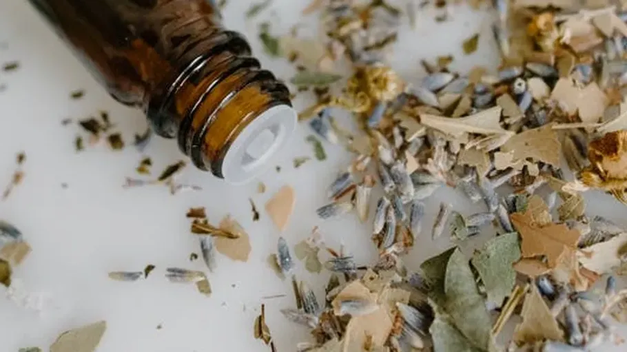 Braune Flasche neben verstreuten getrockneten Kräutern.