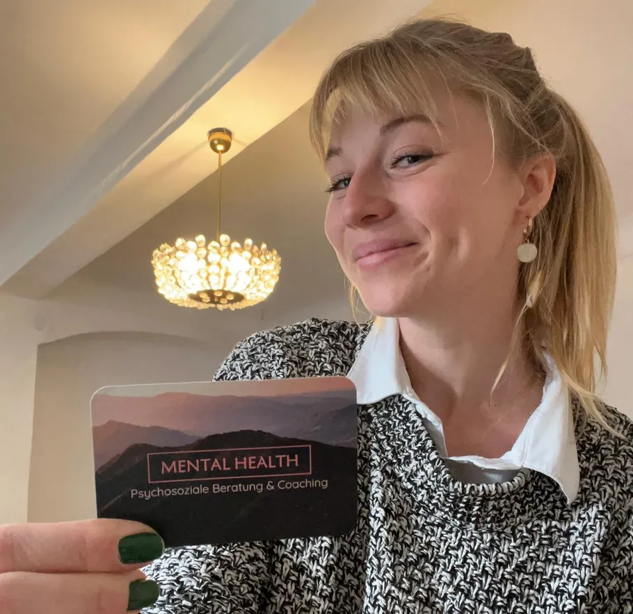 Person smiling holding mental health card indoors.