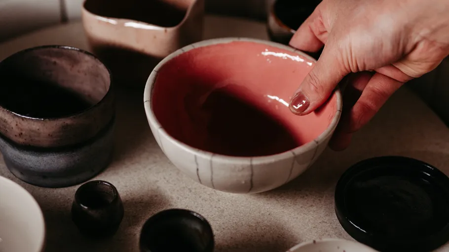 Hand holding ceramic bowl among other pottery.