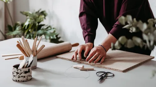 Person working with clay on table, surrounded by tools.