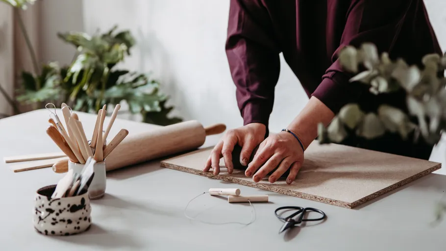 Person working with clay on table, surrounded by tools.