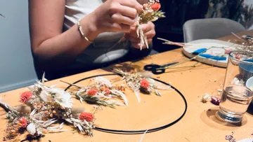 Person bastelt Blumendekoration auf Tisch.