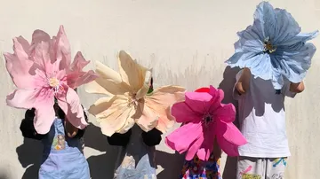 Children holding large paper flowers against wall.