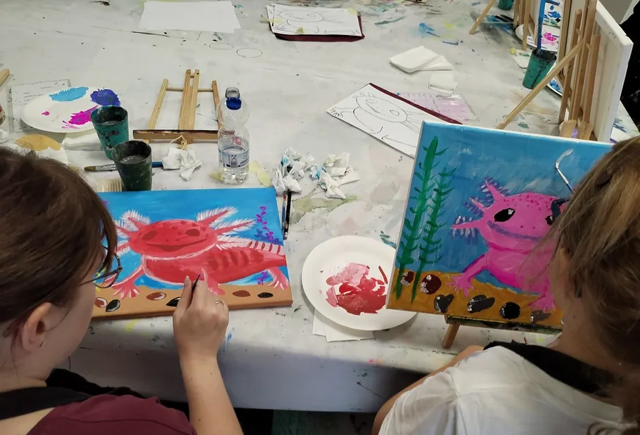 Zwei Personen malen bunte Axolotl auf Leinwänden.