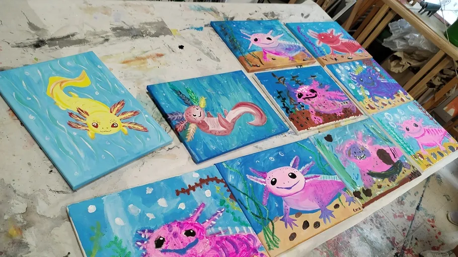 Colorful axolotl paintings on a messy table.