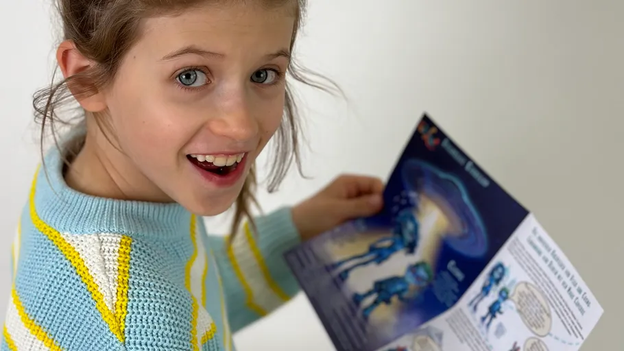Girl smiling, holding a pamphlet, indoors.