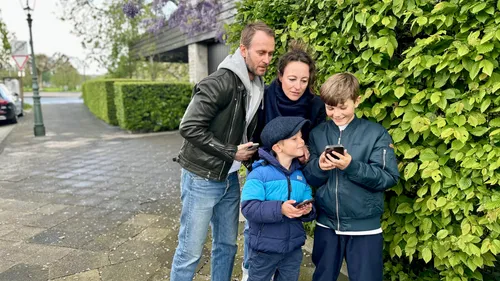 Familie benutzt Smartphones draußen an grüner Hecke.