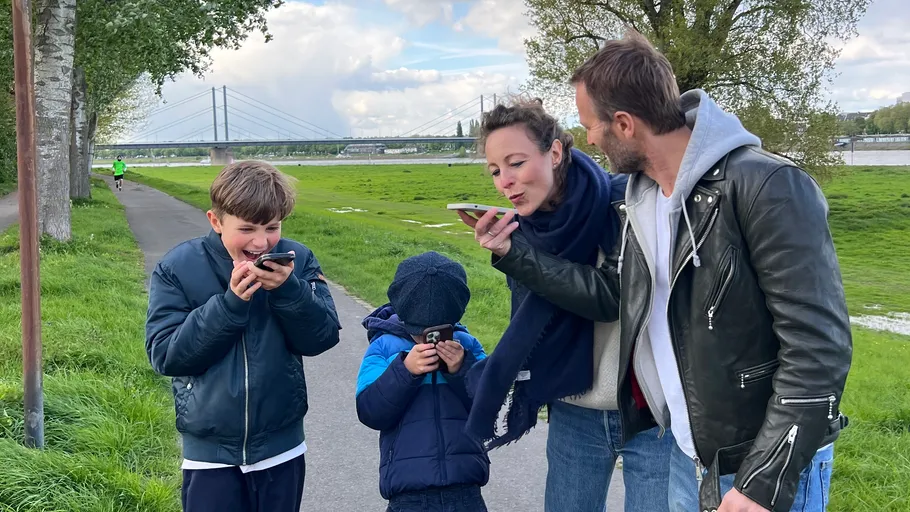 Family enjoying phone games on riverside walkway.