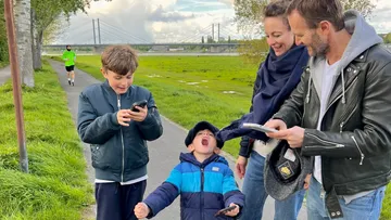 Family enjoying smartphones on riverside path.