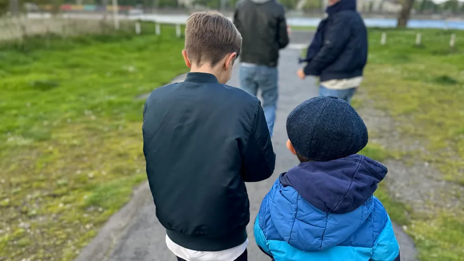 Two boys walking, adults ahead, grassy path.