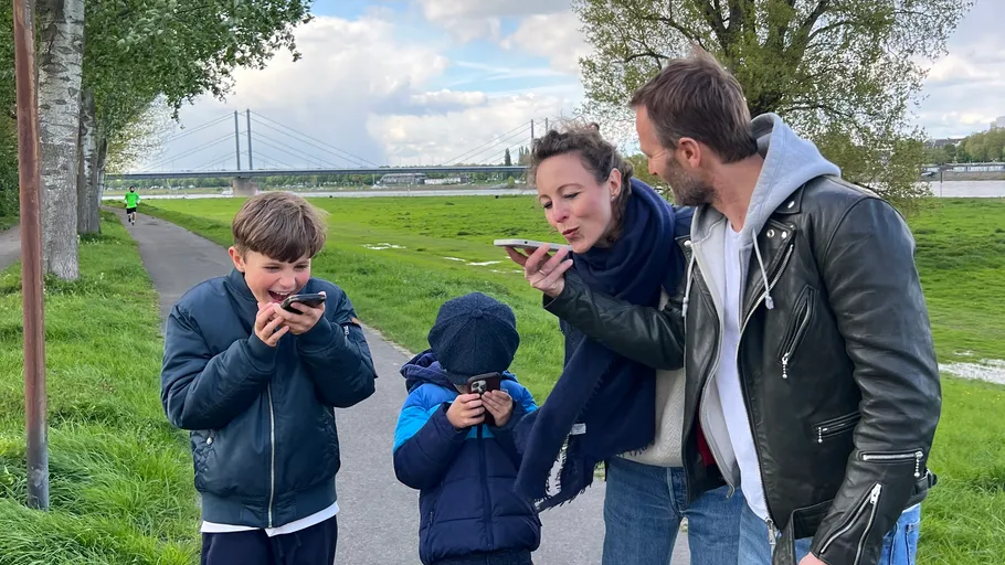 Familie nutzt Handys draußen nahe Brücke.